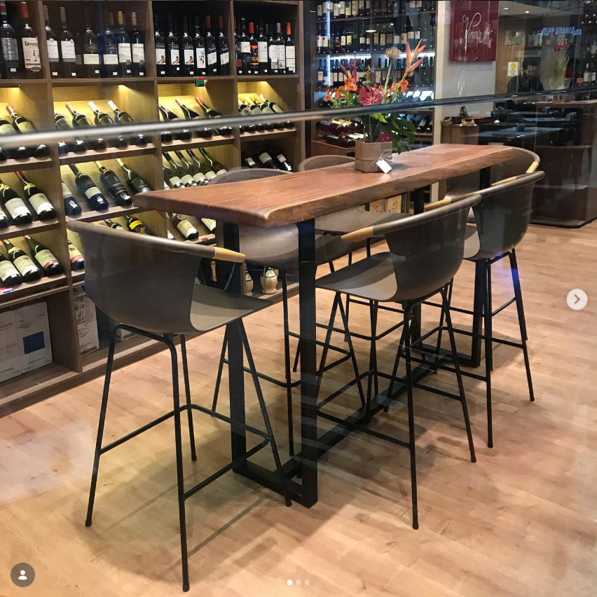 Interior da Vineria 14 com mesa de madeira, banquetas e estantes de vinhos iluminadas